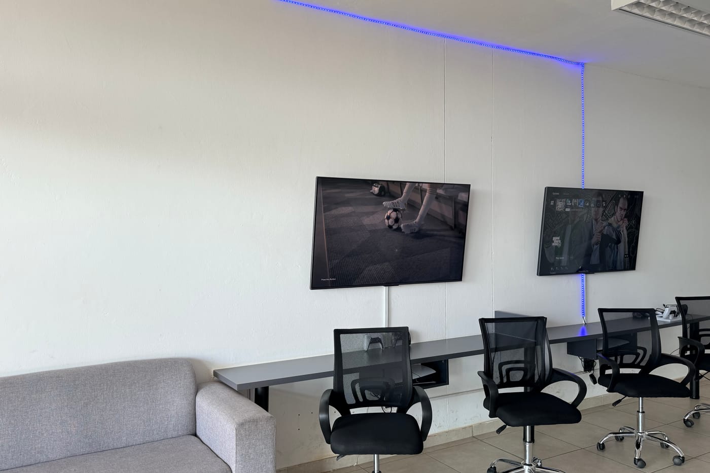 The gaming lounge inside Shop 6 — sofa, desk run, office chairs and two wall-mounted screens