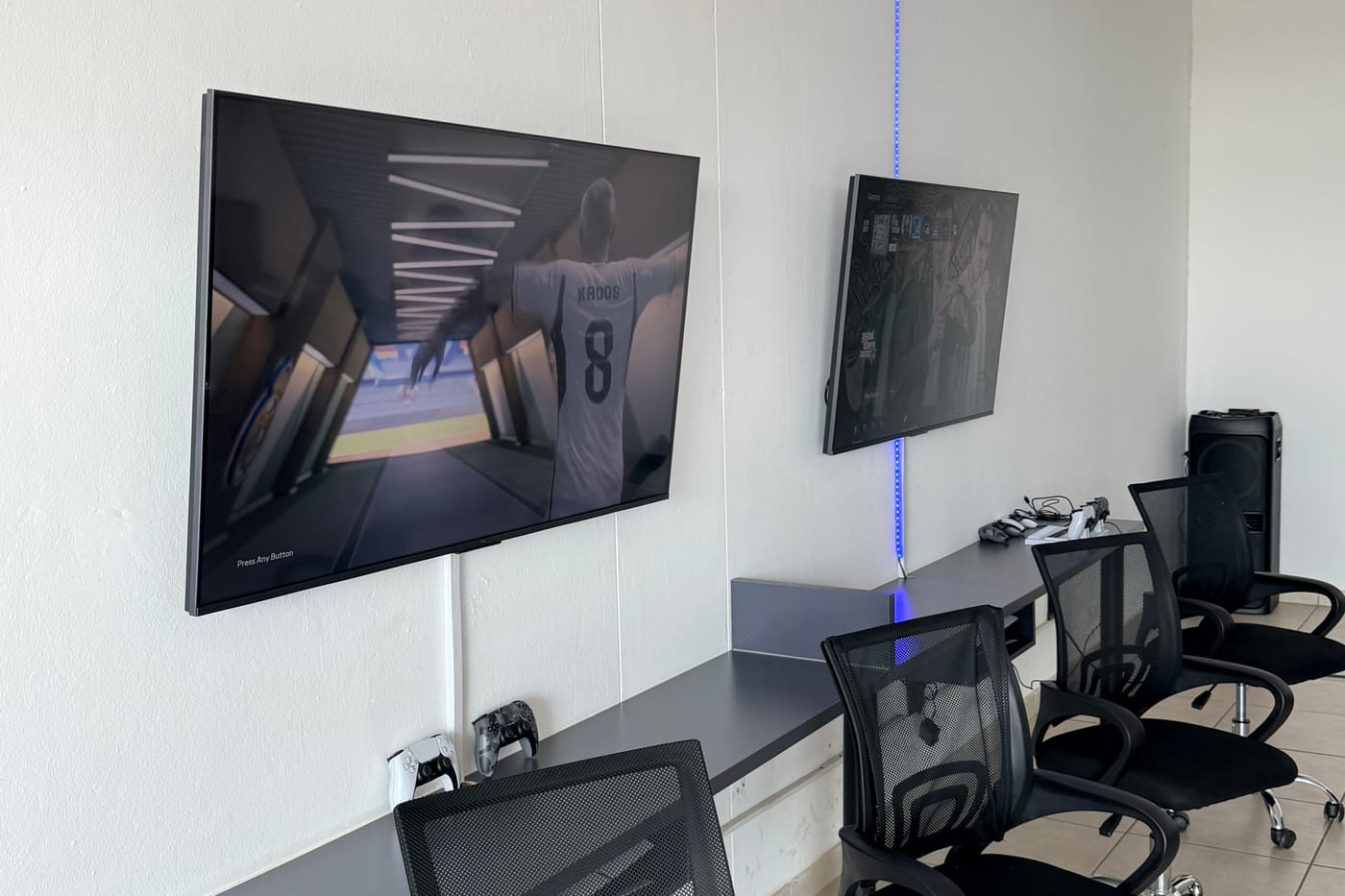 PS5 consoles and controllers on the lounge desk, with FC26 and GTA on the screens