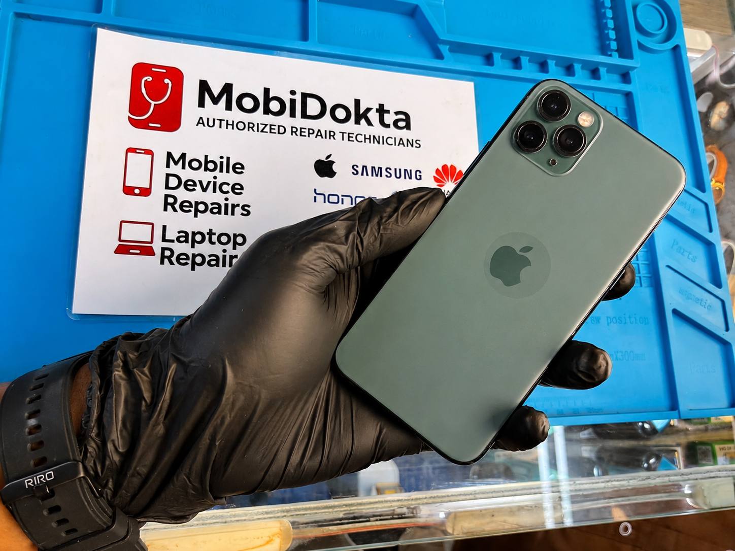 A technician holding a repaired iPhone 11 Pro over the MobiDokta repair bench