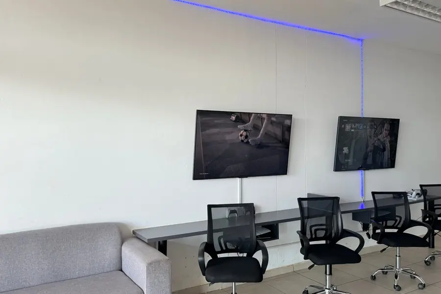 The gaming lounge inside Shop 6 — sofa, desk run, office chairs and two wall-mounted screens